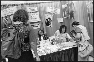 The photo is of the Montreal Health Press at a conference booth table, Toronto, 1992. Photo taken by Judith Lermer Crawley.