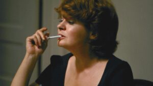 Still from the film "Souris, tu m'inquiètes" featuring a white woman with short brown hair holding a cigarette in her mouth.