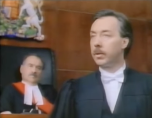 Still from the film "Conspiracy of Silence" featuring a judge and a lawyer, both middle aged white men with moustaches, in a courtroom.