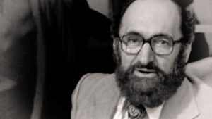 Still from the film "Democracy on Trial" featuring a black and white headshot of Henry Morgentaler, a middle aged white man with a beard and glasses.