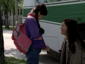 Still from the film "For Angela" featuring Angela Saskosky and her mother, Rhonda Gordon, outside of a bus. Angela, a young Indigenous girl, is hanging her head and her mother, an Indigenous woman in her thirties, is on her knees talking to her.