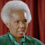 Still from the film "No Way! Not Me" featuring Rosemary Brown, an older Black woman with white cropped hair wearing a teal shirt, speaking on a stage.