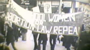 Still from "Women in Struggle" featuring blurry archival footage of women holding a banner that says "Women for Abortion Law Repeal."