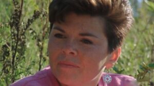 Still from the film "Doctor, Lawyer, Indian Chief" featuring a close-up of Carol Geddes, an Indigenous woman with short cropped brown hair, in a field.