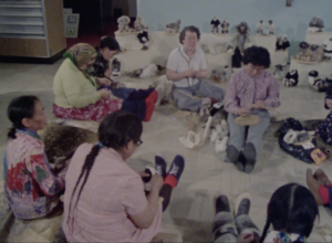 Still from "Mother of Many Children" featuring a group of older Inuit women sitting on the floor in a circle and weaving.