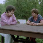 Still from the film "A Mother and Daughter on Abortion" featuring two white women, one older and one younger, with short brown hair talking at a picnic table outdoors.