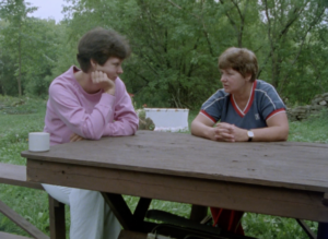 Still from the film "A Mother and Daughter on Abortion" featuring two white women, one older and one younger, with short brown hair talking at a picnic table outdoors.