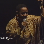 Screenshot of Lillian Allen, a Black woman with short hair wearing a yellow and brown blouse, performing Birth Poem on stage.