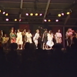 Still of Lillian Allen performing The Subversives. She is joined on stage by many women, who are all dancing.