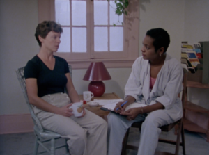 Still from "Sylvie's Story" depicting Sylvie, a white woman with short brown hair, speaking to a shelter worker, a black woman with short black hair.