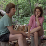 Still of filmmaker Michael Rubbo and Margaret Atwood sitting on tree stumps and talking at a campsite beside a row of her books.