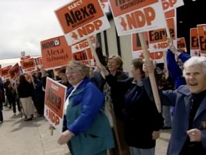 Still from the film "Why Women Run" depicting several elderly white women enthusiastically raising campaign signs that say "Elect Alexa McDonough NDP."