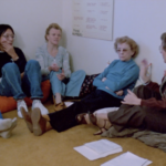 Still from the film "Turnaround" featuring four white women of varying ages sitting on the ground talking.