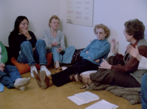 Still from the film "Turnaround" featuring four white women of varying ages sitting on the ground talking.