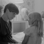 Black and white still from the film "Mother-to-be" featuring a white woman with short hair talking to her young daughter.