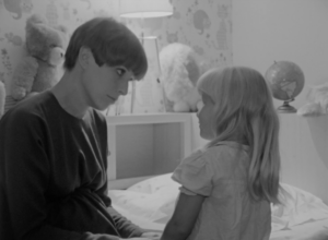 Black and white still from the film "Mother-to-be" featuring a white woman with short hair talking to her young daughter.