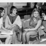 Group of four women sitting in chairs, talking at a women's conference held in Sault Ste. Marie i the 1970s. One is holding a notebook.