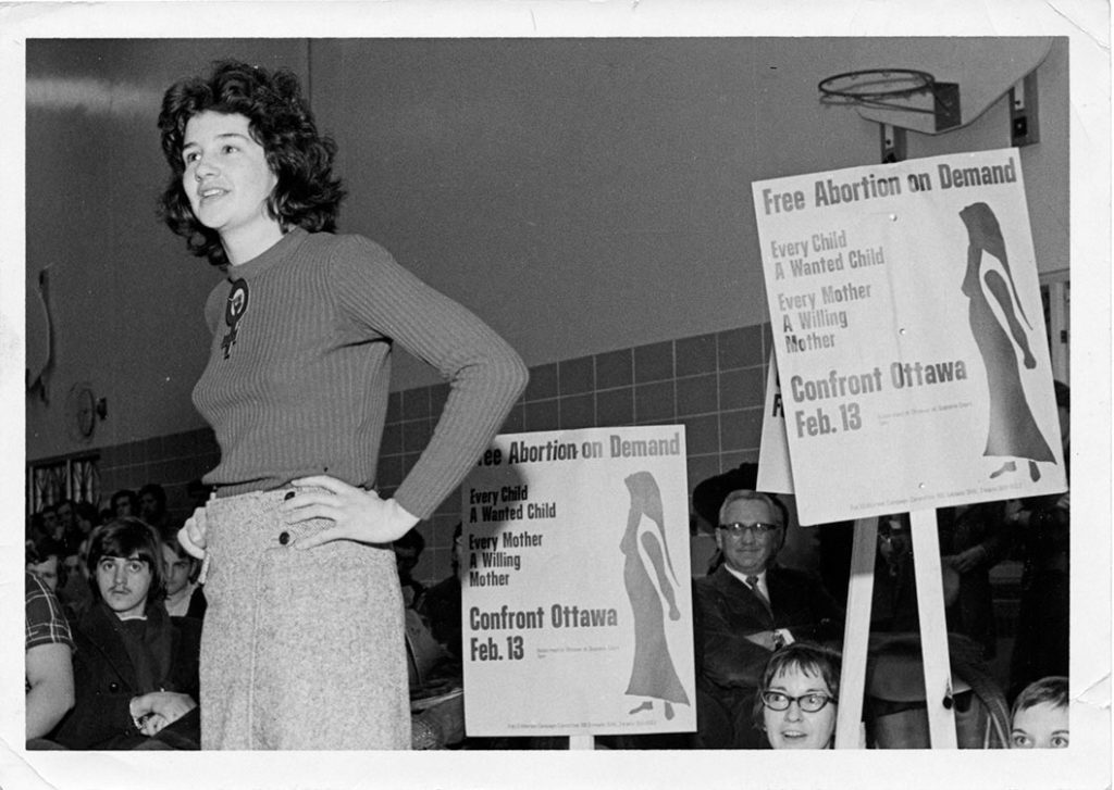 Paula Fletcher (left) standing in a crowd with signs demanding free abortion during a protest in Sault Ste. Marie in 1971.