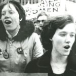 Group of women marching, banner in the background.