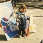 Photo taken of a child standing in front of a poster at the 1985 Vancouver International Women's Day Event.