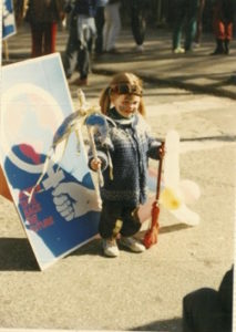 Photo taken of a child standing in front of a poster at the 1985 Vancouver International Women's Day Event.