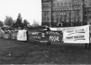 Photo of one section of the Banner Project showing CUPE 2424 slogans including "Tory Economics = Working Poor" as well as the Women's Centre, St. Thomas University's "Fight Sexism; Fight Racism". Women's groups across Canada were asked to produce a protest banner that would become part of a huge banner in Ottawa. The goal was to show the strength and solidarity of women during the Third Commonwealth meeting of Ministers Responsible for Women’s Affairs in October 1990.