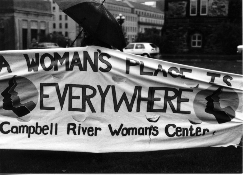 Photo of the Campbell River Woman's Center banner with the slogan "A Woman's Place is Everywhere". Women's groups across Canada were asked to produce a protest banner that would become part of a huge banner in Ottawa. The goal was to show the strength and solidarity of women during the Third Commonwealth meeting of Ministers Responsible for Women’s Affairs in October 1990.