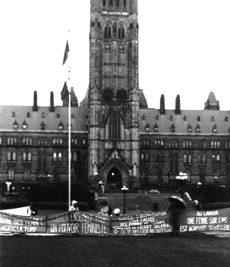 Photo showing several of the banners representing different Québec and francophone women's groups in front of the Parliament Building in Ottawa. They were part of the Banner Project which asked groups across Canada to produce a protest banner that would become part of a huge banner in Ottawa. The goal was to show the strength and solidarity of women during the Third Commonwealth meeting of Ministers Responsible for Women’s Affairs in October 1990.