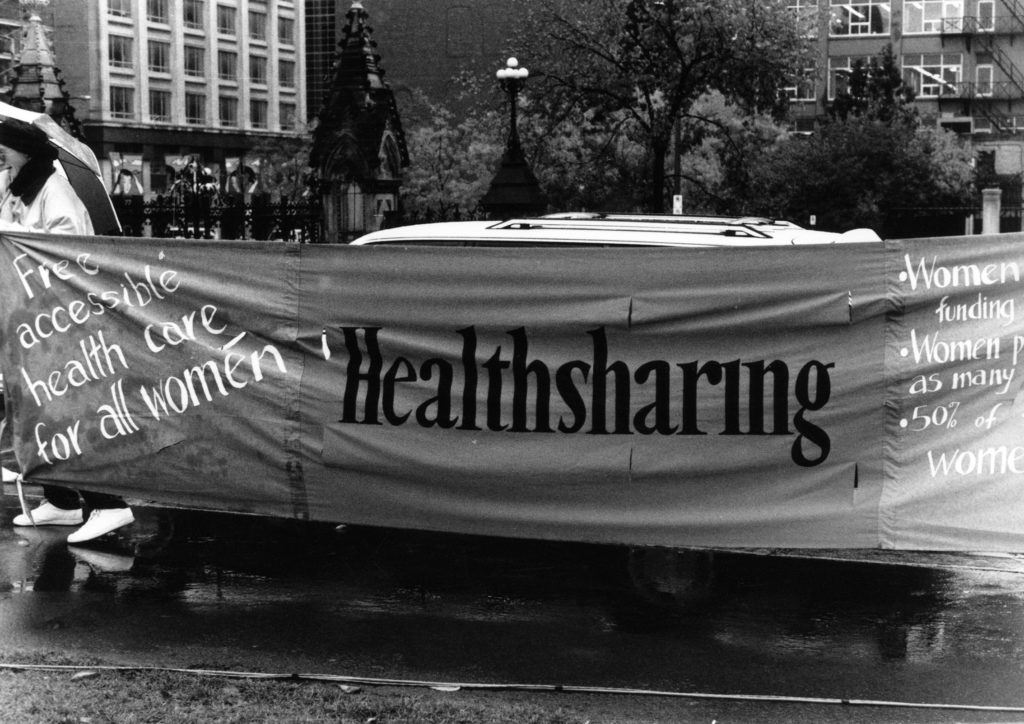 Healthsharing's banner calls for free accessible healthcare for all women. It is one section of a huge banner made up of individual protest messages created by women's groups across Canada. The goal was to show the strength and solidarity of women during the Third Commonwealth meeting of Ministers Responsible for Women’s Affairs in October 1990.