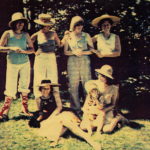 Scanned photograph of six members of Isis collective in a garden. Four members are standing and two are sitting on the ground.