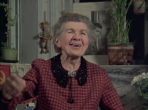 Still from the film "Portrait of the Artist--As an Old Lady" featuring Paraskeva Clark, an elderly white woman with grey hair wearing a red checkered blouse, singing animatedly.