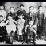 Still from the film "Under the Willow Tree" featuring a black and white archival photo of a Chinese family formally dressed. There is a mother and a father and eight young children.