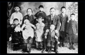 Still from the film "Under the Willow Tree" featuring a black and white archival photo of a Chinese family formally dressed. There is a mother and a father and eight young children.