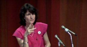 Film still from "If You Love This Planet" of Dr. Helen Caldicott speaking into a microphone on a stage.