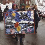 This photo taken at an IWD March in Toronto shows the Black Women's Collective and their banner, as well as Women Against the Arms Race.