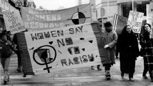 The theme of the Toronto International Women's Day March was Say No to Racism. The photo shows the Native Women's Resource Centre banner and contingent, as well as placards highlighting the impact of racism and colonialism on children. Photograph by Diana Meredith.