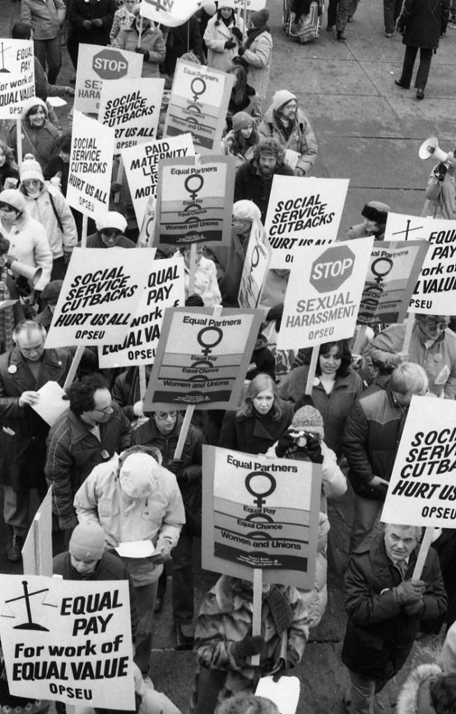 The Ontario Public Service Employees Union (OPSEU) contingent march at the 1983 International Women's Day March in Toronto carry placards carry calling for equal pay, paid maternity leave, ending sexual harassment, and social service cuts.