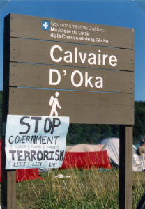 This photo is one of a number taken at the Oka Peace Camp set up in July 1990 in solidarity with the Mohawks of Kanehsatake who rose up in defense of their ancestral lands after the Oka Golf Club proposed an extension and the building of luxury condos over a Mohawk ancestral graveyard in the sacred wooded area known as “The Pines”. This land had never been ceded. In early July, after the Mohawks refused to end their non-violent occupation of the area or to take down the barricade, the Sûreté du Québec (Quebec police) moved in resulting in a violent confrontation. Later, the Canadian army was called in. Mohawk women, including Ellen Gabriel, played a central role in the uprising, which lasted for 78 intense days (July 11 – September 26, 1990). In the end, the golf course was not extended, and the condos were not built. But the larger issues of land sovereignty have never been resolved.