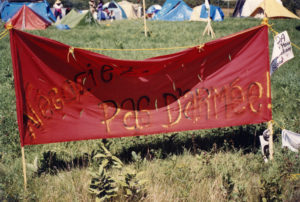 This photo is one of a number taken at the Oka Peace Camp set up in July 1990 in solidarity with the Mohawks of Kanehsatake who rose up in defense of their ancestral lands after the Oka Golf Club proposed an extension and the building of luxury condos over a Mohawk ancestral graveyard in the sacred wooded area known as “The Pines”. This land had never been ceded. In early July, after the Mohawks refused to end their non-violent occupation of the area or to take down the barricade, the Sûreté du Québec (Quebec police) moved in resulting in a violent confrontation. Later, the Canadian army was called in. Mohawk women, including Ellen Gabriel, played a central role in the uprising, which lasted for 78 intense days (July 11 – September 26, 1990). In the end, the golf course was not extended, and the condos were not built. But the larger issues of land sovereignty have never been resolved.