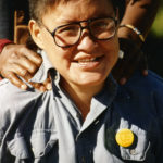 This photo is one of a number taken at the Oka Peace Camp set up in July 1990 in solidarity with the Mohawks of Kanehsatake who rose up in defense of their ancestral lands after the Oka Golf Club proposed an extension and the building of luxury condos over a Mohawk ancestral graveyard in the sacred wooded area known as “The Pines”. This land had never been ceded. In early July, after the Mohawks refused to end their non-violent occupation of the area or to take down the barricade, the Sûreté du Québec (Quebec police) moved in resulting in a violent confrontation. Later, the Canadian army was called in. Mohawk women, including Ellen Gabriel, played a central role in the uprising, which lasted for 78 intense days (July 11 – September 26, 1990). In the end, the golf course was not extended, and the condos were not built. But the larger issues of land sovereignty have never been resolved.