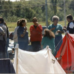 This photo is one of a number taken at the Oka Peace Camp set up in July 1990 in solidarity with the Mohawks of Kanehsatake who rose up in defense of their ancestral lands after the Oka Golf Club proposed an extension and the building of luxury condos over a Mohawk ancestral graveyard in the sacred wooded area known as “The Pines”. This land had never been ceded. In early July, after the Mohawks refused to end their non-violent occupation of the area or to take down the barricade, the Sûreté du Québec (Quebec police) moved in resulting in a violent confrontation. Later, the Canadian army was called in. Mohawk women, including Ellen Gabriel, played a central role in the uprising, which lasted for 78 intense days (July 11 – September 26, 1990). In the end, the golf course was not extended, and the condos were not built. But the larger issues of land sovereignty have never been resolved.