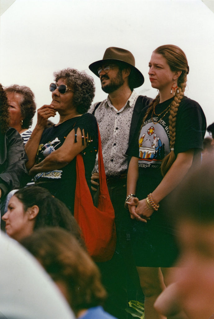 This photo is one of a number taken at the Oka Peace Camp set up in July 1990 in solidarity with the Mohawks of Kanehsatake who rose up in defense of their ancestral lands after the Oka Golf Club proposed an extension and the building of luxury condos over a Mohawk ancestral graveyard in the sacred wooded area known as “The Pines”. This land had never been ceded. In early July, after the Mohawks refused to end their non-violent occupation of the area or to take down the barricade, the Sûreté du Québec (Quebec police) moved in resulting in a violent confrontation. Later, the Canadian army was called in. Mohawk women, including Ellen Gabriel, played a central role in the uprising, which lasted for 78 intense days (July 11 – September 26, 1990). In the end, the golf course was not extended, and the condos were not built. But the larger issues of land sovereignty have never been resolved.