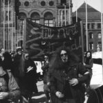 On an International Women's Day March in front of Queen's Park, marchers carry the banner "Still Ain't Satisfied".