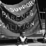 Photo taken at a Queen's Park protest showing a young girl in front of banner for Sole Support Parents Coalition.