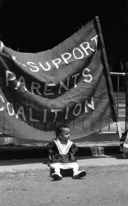 Photo taken at a Queen's Park protest showing a young girl in front of banner for Sole Support Parents Coalition.