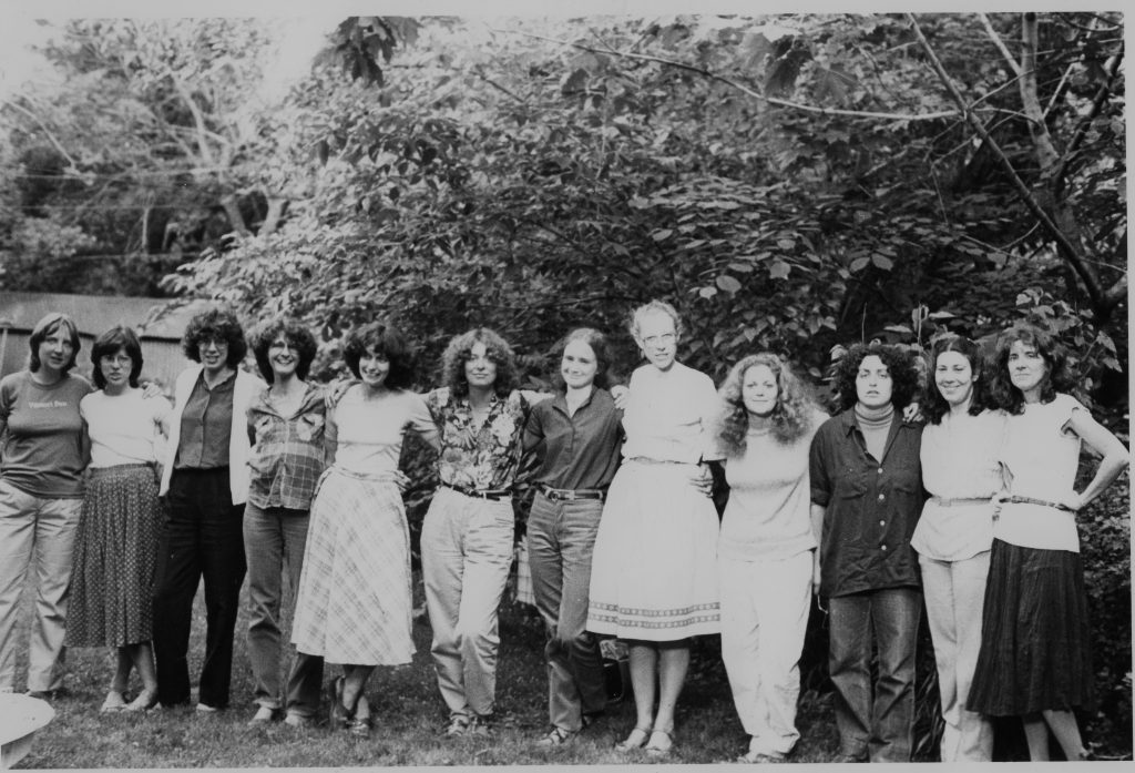 This is an undated group photo of the members of Women's Press. From left to right: Meg Luxton, Peggy McDonough, Brenda Roman, Naomi Wall, Lois Pike, Jane Springer, Daphne Read, Judy Skinner, Margie Wolfe, Connie Guberman, Wendy Donner, Judy (McClard) Blankenship