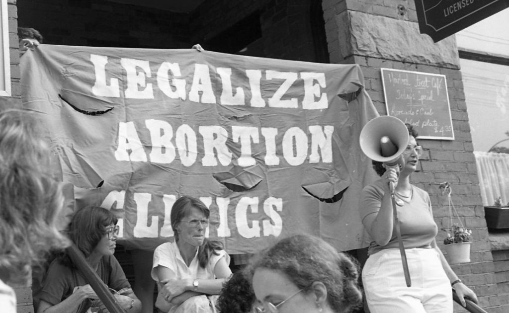 Judy Rebick stands in front of a Legalize Abortion Clinics banner holding a megaphone at a Toronto support rally outside the Morgentaler Clinic in 1983.