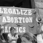 Judy Rebick stands in front of a Legalize Abortion Clinics banner holding a megaphone at a Toronto support rally outside the Morgentaler Clinic in 1983.