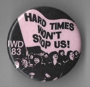 This button for International Women's Day 1983 features the slogan "Hard Times Won't Stop Us".