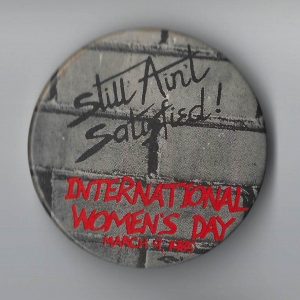 The theme of this button for the 1985 International Women's Day March and Rally in Toronto is Still Ain't Satisfied!